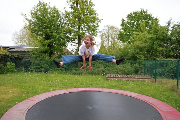 A teenage girl with glasses does a split while jumping on a trampoline